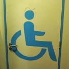 Voor de aanduiding van het aangepast toilet wordt er gebruik gemaakt van het rolstoel-pictogram. Het pictogram heeft een contrasterende kleur ten opzichte van de kleur van het deurblad. (Jeugdcentrum Ahoy, Wijnegem)