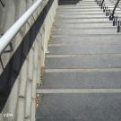 De trap is voorzien van een leuning aan beide zijden. Optimaal wordt de leuning op twee hoogten voorzien en loopt ze 40cm voorbij het begin en einde van de trap. Elke trede is voorzien van een contrastmarkering gecombineerd met een anti-slip materiaal. (Jeugdhuis Bascule, Eversel)